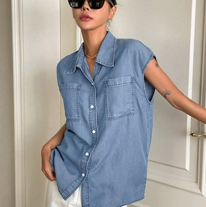 Detail of light blue denim shirt with sleeveless cut, twin pockets and white buttons