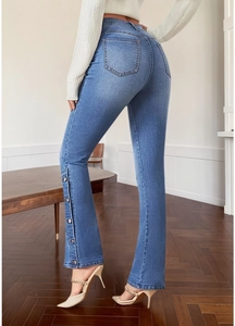 Detail view of high waist flared jeans with side metal button slits and blue wash texture