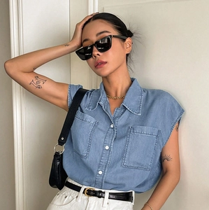 Close-up of women's light blue sleeveless denim shirt with front pockets and white buttons