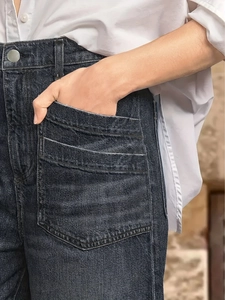 Detail of dark wash denim jeans showing metallic button and multi-layered stitched pockets