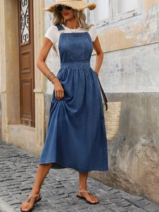 Detail of dark blue denim overall dress featuring large bib pocket and cinched waist design