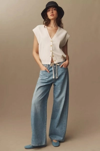 Full-body shot of light blue wide-leg jeans styled with a white vest and black knit bucket hat