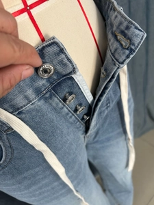 Detail of high-waist light blue denim jeans with four embossed metal buttons and drawstring