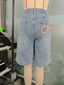 Détail d'un short en jean bleu clair avec un motif de nœud orange sur la poche