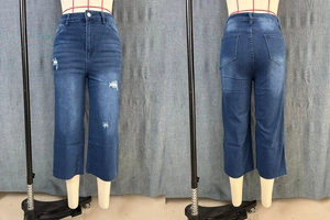 Detail view of high-waisted distressed denim culottes with ripped effects and raw hem