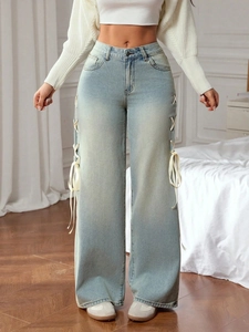 Detail of light blue wide-leg jeans featuring decorative side hollow-out ribbon tie bows