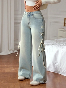 Detail of high waisted wide leg light blue jeans with side ribbon bow tie design