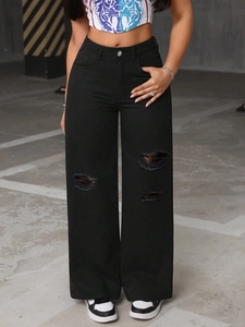 Detail of high-waisted wide leg black distressed jeans with knee rips in industrial setting