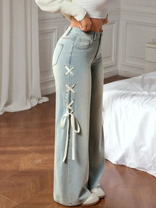 Detail of light blue wide-leg jeans featuring decorative side ribbon lace-up design