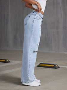 Detail view of high-waisted distressed light blue denim jeans with ripped knee design