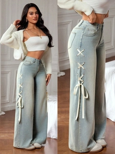 Detail of light blue wide-leg jeans featuring decorative white side ribbons and bows