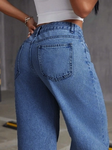 Detail view of high-waist straight jeans back pocket and stitching on washed denim fabric