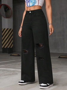 Detail of high-waisted black wide-leg jeans with ripped knees and street style distressed finish
