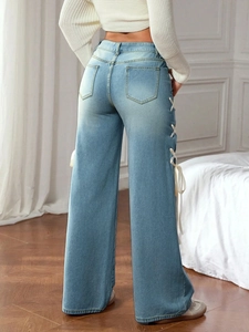 Detail of high-waisted light blue jeans featuring cream ribbon lace-up sides and back pockets