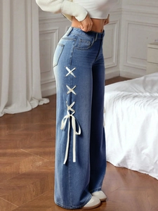 Detail of wide leg denim jeans with white ribbon lace-up bows on the side seam
