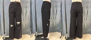 Detail view of black high-waisted wide-leg jeans with distressed knee holes and loose fit