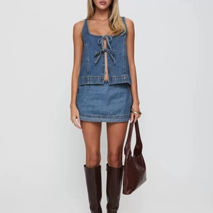 Détail d'un ensemble denim bleu deux pièces avec haut à lacets, nœuds et mini-jupe assortie