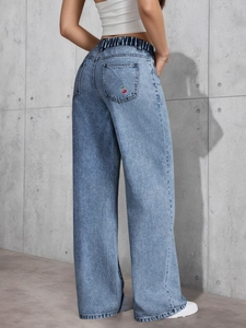 Detailed close-up of red cherry embroidery on the back pocket of blue wide-leg jeans