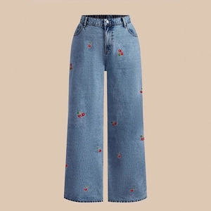 Detail of high waisted blue denim jeans with red cherry embroidery and wide leg cut