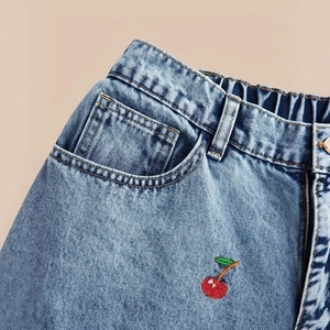 Detail of light blue denim pants with elastic waist and delicate cherry embroidery