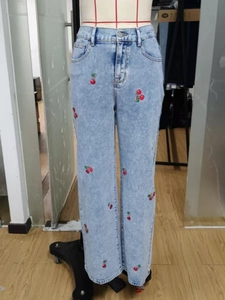 Detail of red cherry embroidery and wash texture on light blue high-waist denim pants