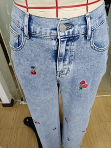 Detailed view of red cherry embroidery on light blue high-waisted denim jeans