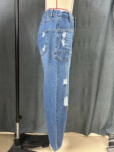 Detail of ripped blue denim jeans with elastic waistband and distressed holes on mannequin