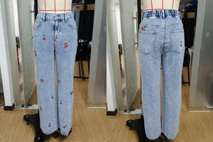 Detail of red cherry embroidery on light blue wide-leg denim jeans with elastic waist