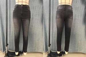 Detail of slim-fit black jeans featuring raw fringe hems and washed grey denim texture