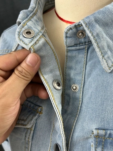 Macro shot of light blue denim jacket collar with textured metal buttons and neat stitching