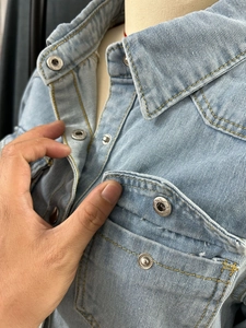 Detail of light blue denim shirt showing snap buttons, yellow stitching, and chest pocket