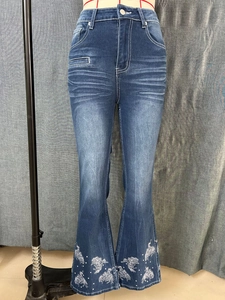 Detail of embroidered horse pattern and silver studs on flared blue denim jeans