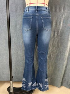 Detail of embroidered floral patterns on flared hem of dark blue denim jeans