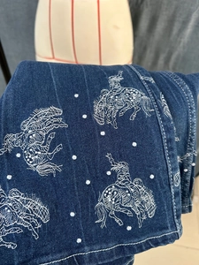 Close-up of white western cowboy embroidery on dark blue stretch denim fabric