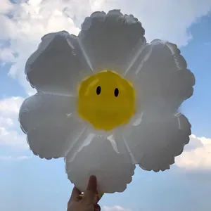 Detail of white daisy foil balloon with a yellow smiley face held against the sky