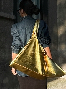 Sac fourre-tout triangle doré minimaliste porté par un mannequin en milieu urbain