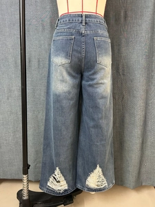 Detail van de gescheurde zoom op een blauwe high-waist jeans met wijde pijpen en franje