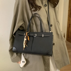 Minimalist black tote bag with strap buckle and wood bead charm shown on trench coat