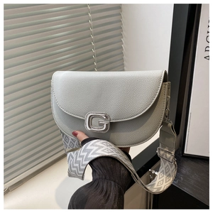 Detail of light gray textured leather saddle bag with rhinestone G buckle and woven strap