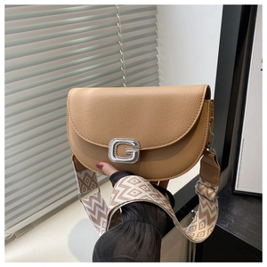 Close-up of brown saddle bag featuring a sparkling G-buckle and woven geometric strap