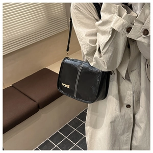 Detail of glossy black shoulder bag with white stitching and gold metal plate