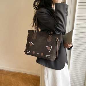 Brown suede tote bag with cartoon cat face design shown on a model in a minimalist room