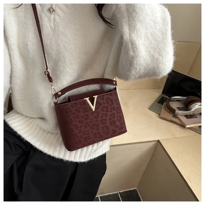 Detail of burgundy leopard embossed mini crossbody bag with a gold V metal clasp