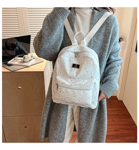 Detailed view of white backpack with silver star print and black metal brand plaque