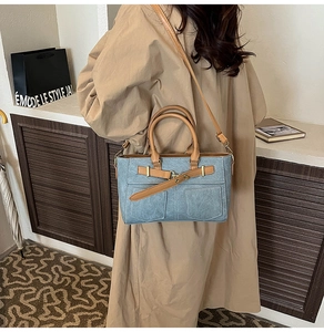 Detail of light blue crossbody bag with brown handles and decorative front pockets