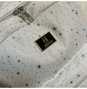 Close-up of white fabric with silver stars and a metallic brand logo with dual zippers