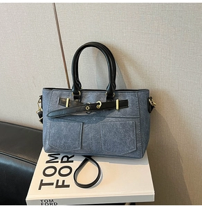 Detail of blue denim handbag with black leather handles and golden metal hardware