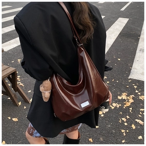 Detail of glossy deep brown tote bag with metal tag and plush bear charm on urban street