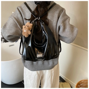 Detail of glossy black hobo bag with teddy bear charm worn as a backpack for women