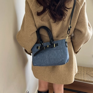 Blue denim crossbody bag with black leather straps worn by a model in a camel coat